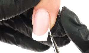 Precyzyjne malowanie białej końcówki french manicure bez użycia pasków. Dłoń w czarnej rękawiczce trzyma pędzelek.
