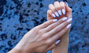 Eleganckie, białe paznokcie z granatowym french manicure, prezentowane na tle niebieskiego, aksamitnego materiału.