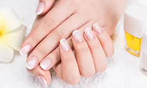 Elegancki manicure french z diamencikami, dłonie zadbane i wypielęgnowane, obok kwiat i lakiery.