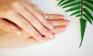 Eleganckie paznokcie french jesienny, delikatnie ułożone dłonie obok zielonego liścia paproci.