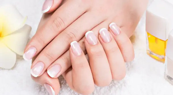 Elegancki manicure french z diamencikami, dłonie zadbane i wypielęgnowane, obok kwiat i lakiery.