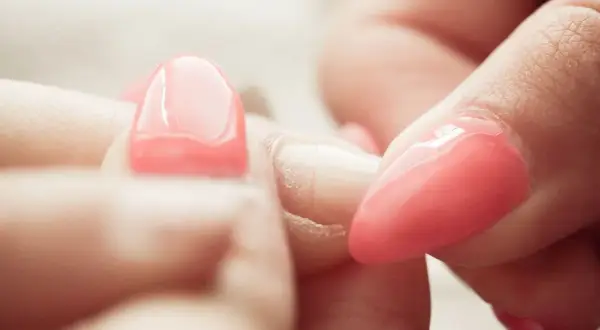 Zbliżenie na dłonie, gdzie widać proces usuwania manicure tytanowego. Różowe paznokcie są w trakcie zdejmowania.