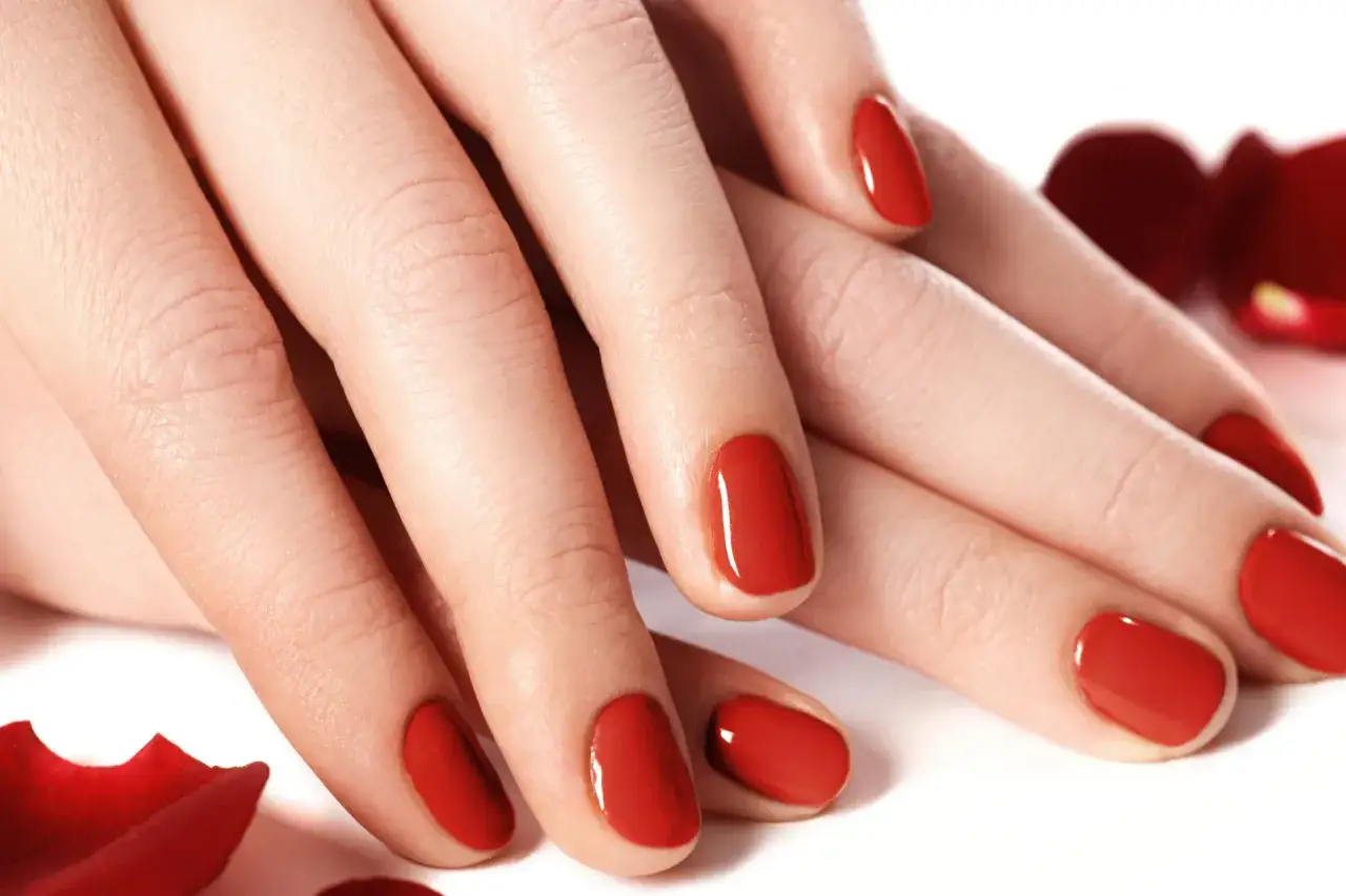 Dłonie z idealnym manicure, czerwone paznokcie wyglądają jak po przedłużaniu paznokci tytanem.