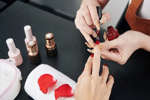 Manicure w trakcie. Stylistka nakłada czerwony lakier. Zastanawiasz się, jak przyspieszyć wysychanie lakieru do paznokci?